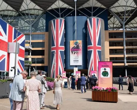 People walk through the Ascot racecourse entrance decorated with Union Jack banners and flower planters.