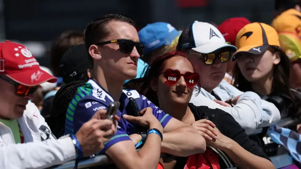 General view of fans ahead of the British Grand Prix. They are leaning on a barrier, wearing dark glasses and baseball caps.