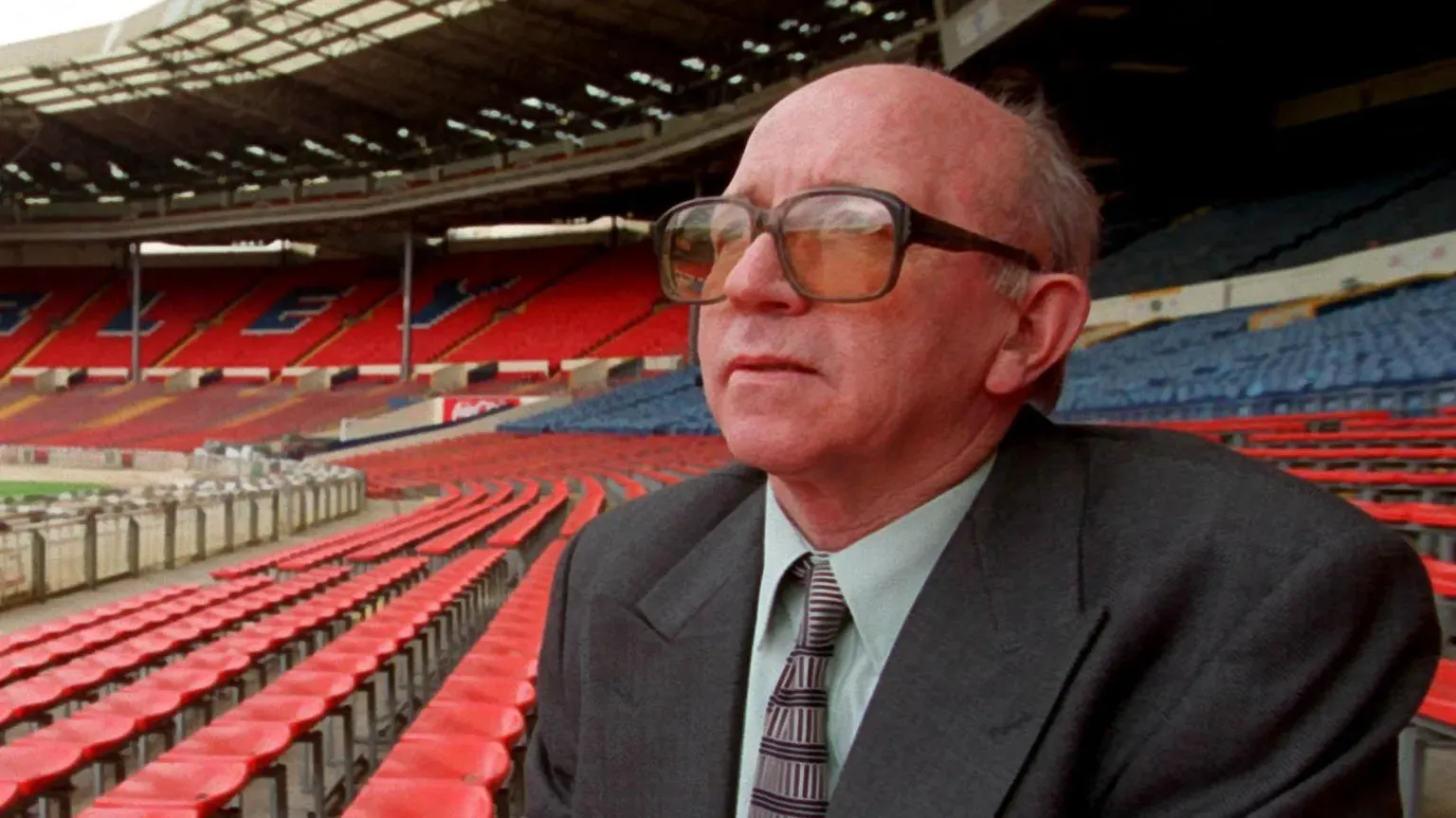 Reuters Nobby Stiles sits in the stands at Wembley. He is wearing a suit and glasses with a yellow tint.