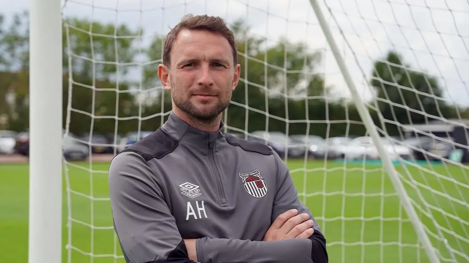 Grimsby Town FC Alex Hughes posing for a picture while standing in a goal wearing a Grimsby Town tracksuit.